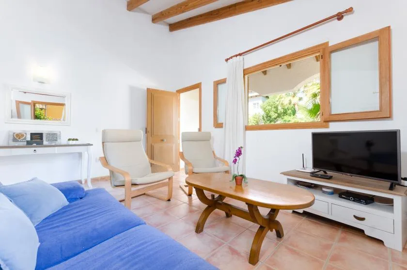Una sala luminosa con asientos azules, una mesa de centro de madera y un televisor.