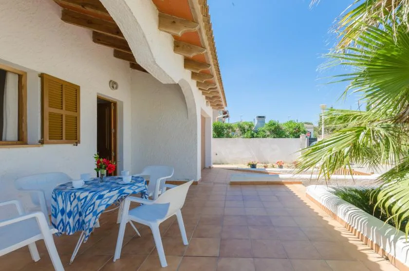 Un patio soleado con suelo de baldosas y asientos junto a un edificio blanco.