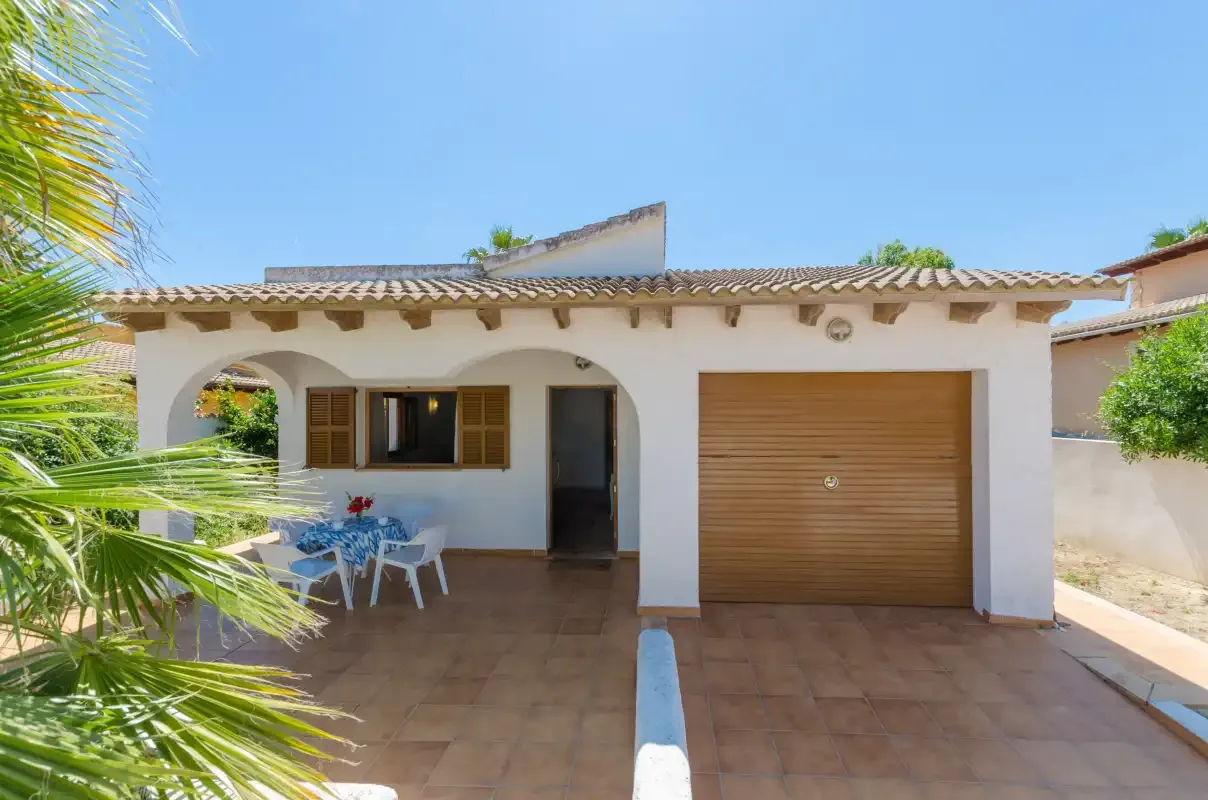 Una casa de una planta con patio de baldosas, asientos al aire libre y la puerta del garaje cerrada.