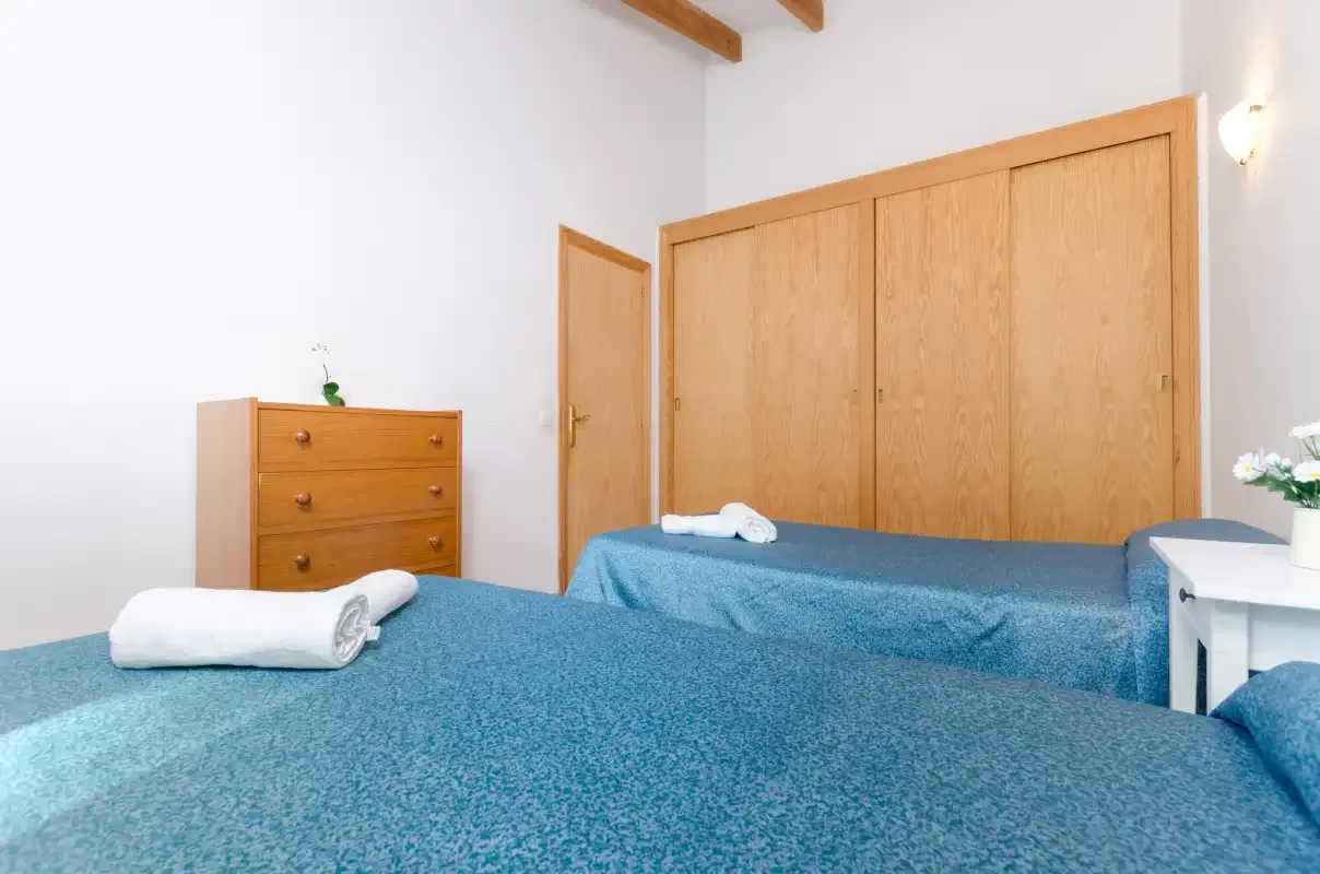 Un dormitorio con ropa de cama azul, una cómoda de madera y un armario.