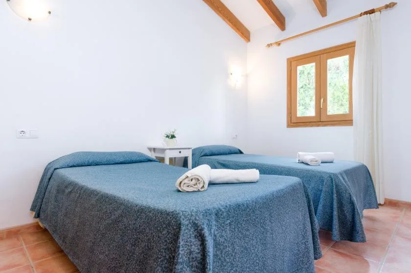 Un dormitorio luminoso con dos camas cubiertas con ropa de cama azul y una ventana.