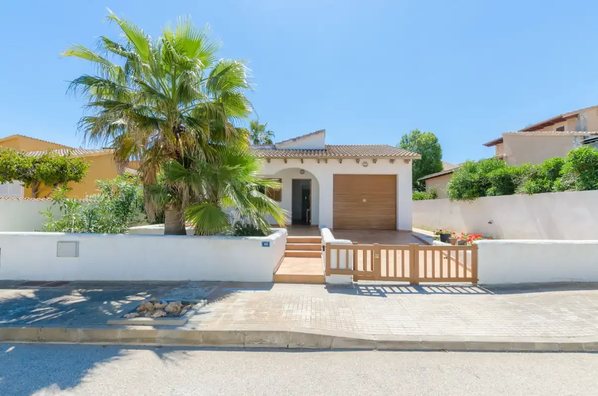 La entrada de una casa con una puerta de madera, un garaje y una palmera.