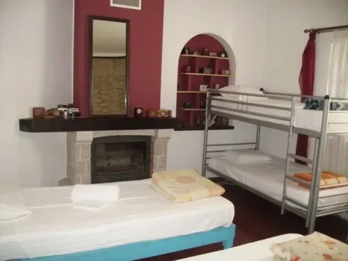 Dormitorio compartido con cama individual, litera metálica, chimenea, estantes en arco y ventanas con vistas al jardín.