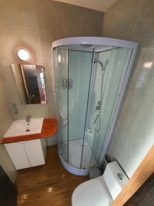 Baño con ducha de esquina, lavabo blanco y encimera roja.