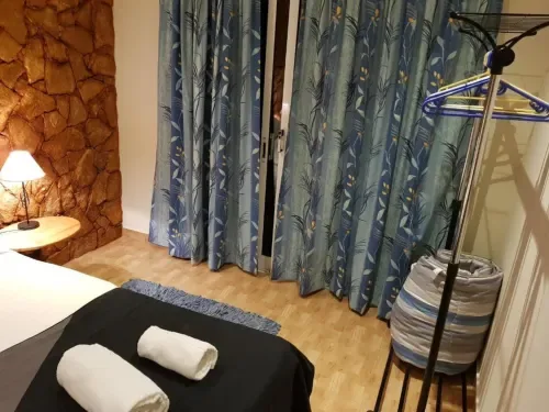 Habitación doble con cama, cortinas azules con estampado floral, suelo de madera y perchero.
