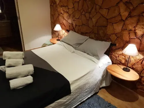 Habitación doble con una pared decorativa de piedra, ropa de cama blanca, cojines grises y luces junto a la cama.