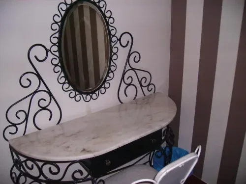 Tocador de metal negro ornamentado con espejo ovalado y encimera de mármol.