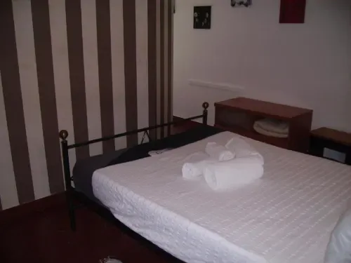 Habitación doble con cama de estructura metálica, ropa de cama blanca, papel pintado a rayas y madera oscura.