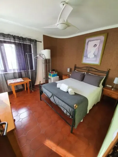 Habitación doble con cama de estructura metálica, suelo de terracota, ventilador de techo y vistas al jardín.