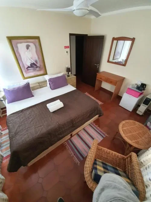 Habitación doble con cama queen, muebles de madera y sillas de ratán.