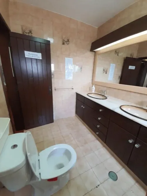Baño compartido con lavabo doble, inodoro y muebles de madera oscura.