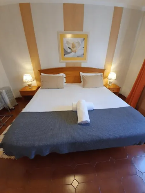 Habitación doble con cama de madera, ropa de cama blanca, manta decorativa azul y lámparas de noche.