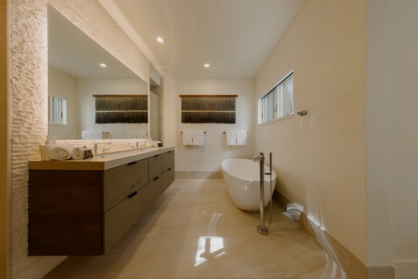 Un baño luminoso con un tocador largo, un espejo grande y una bañera exenta.