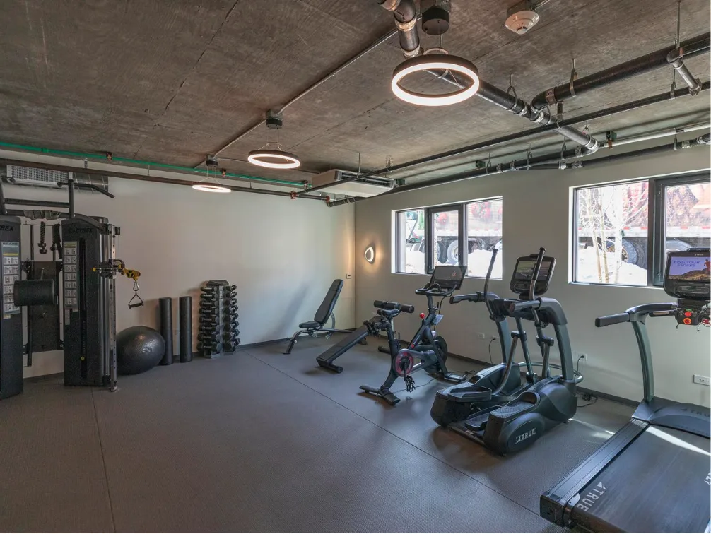 Un gimnasio con máquinas de ejercicio y equipo junto a grandes ventanas.