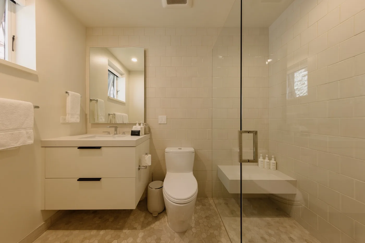 Un baño alicatado con lavabo, espejo, inodoro y panel de ducha de vidrio.