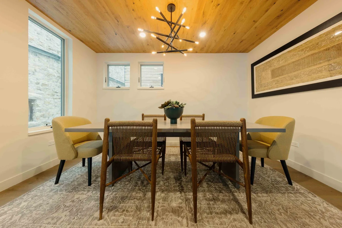 Comedor con una mesa, asientos tejidos y un techo revestido de madera.