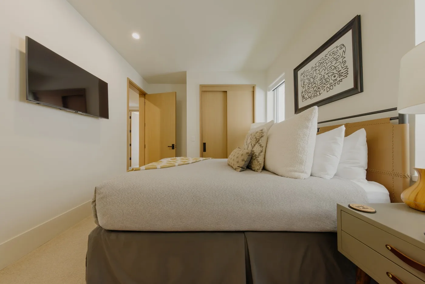 Un dormitorio luminoso con una cama grande, un televisor en la pared y un cuadro enmarcado.