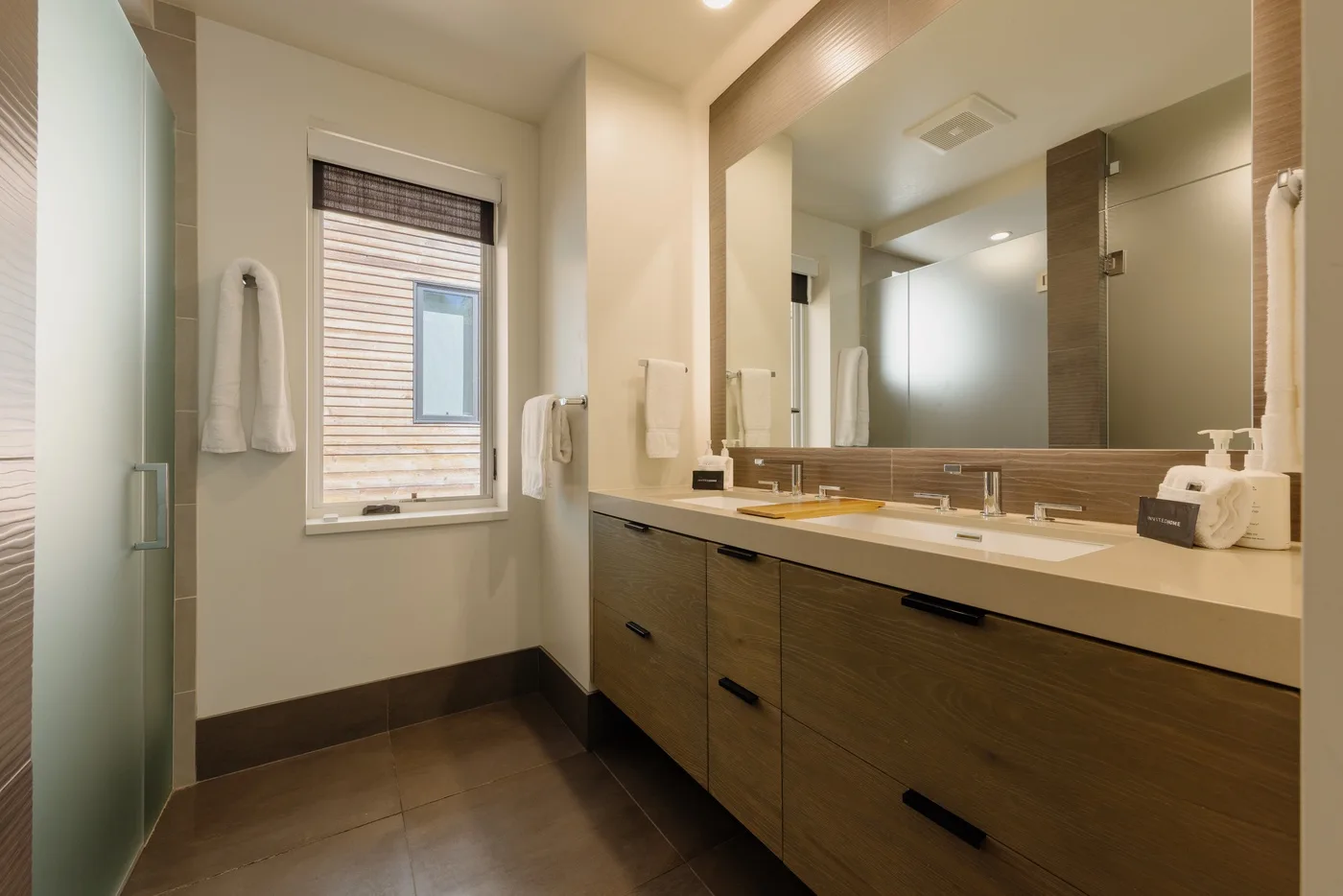 Un lavabo de baño con un espejo amplio y una ventana con persianas.