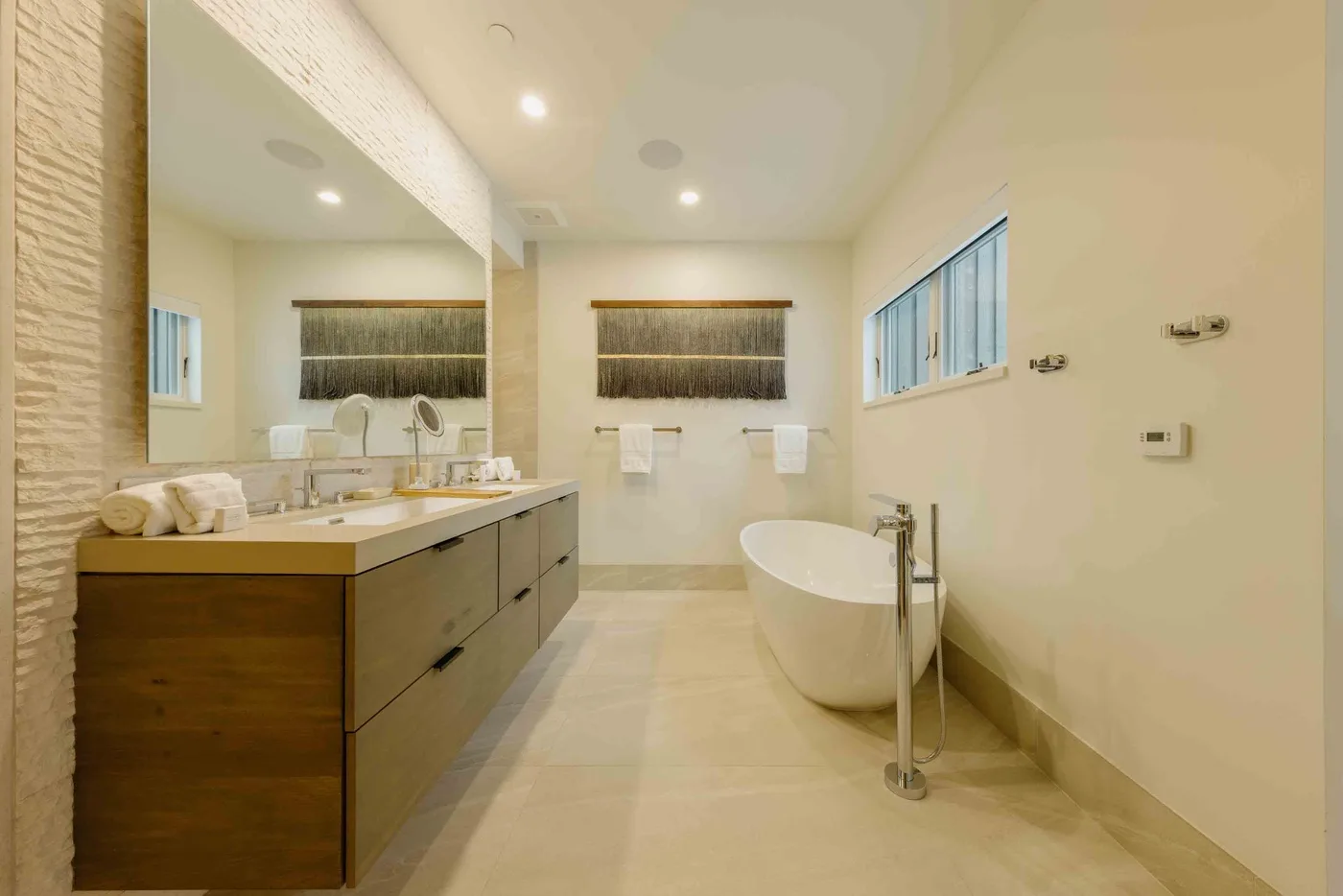 Un baño luminoso con un mueble de lavabo largo, espejo y bañera exenta.