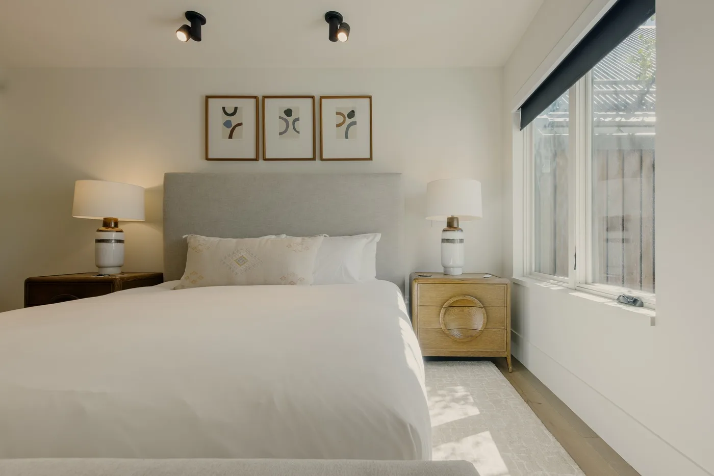 Un dormitorio luminoso con una cama, mesitas de noche y una ventana grande.