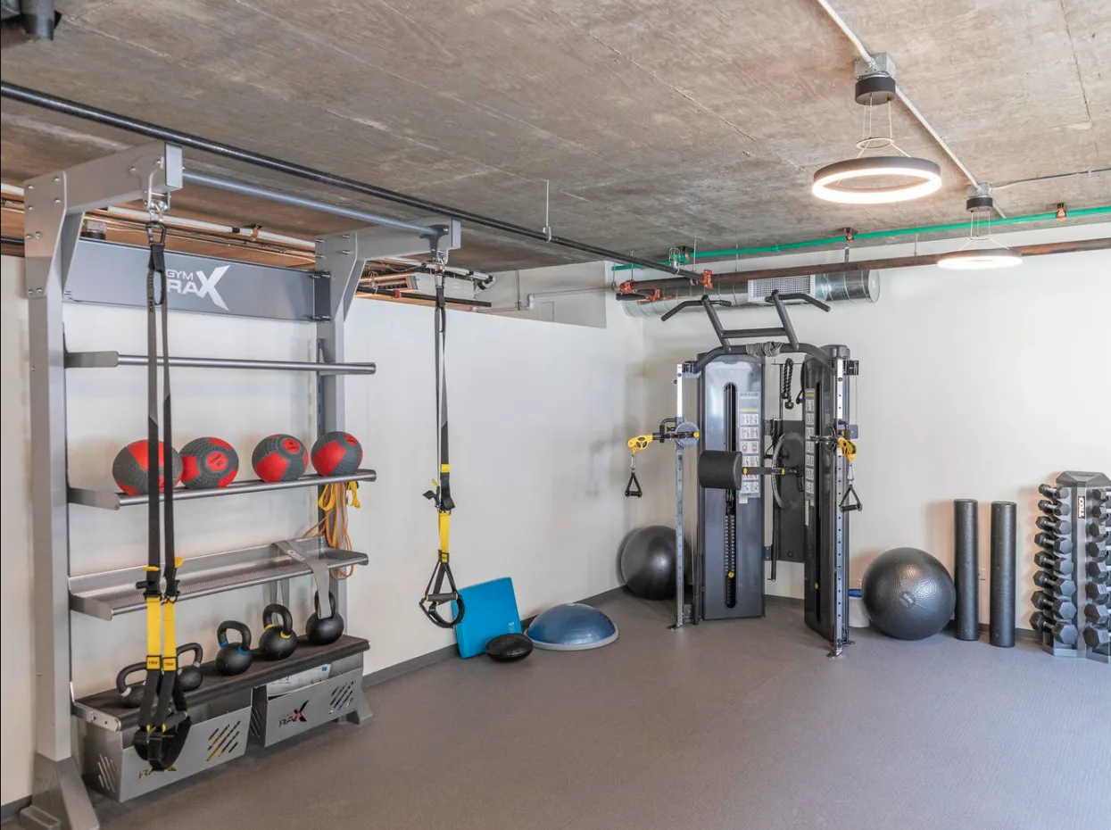 Una sala de entrenamiento con equipos de fuerza, pelotas de ejercicio y pesas.
