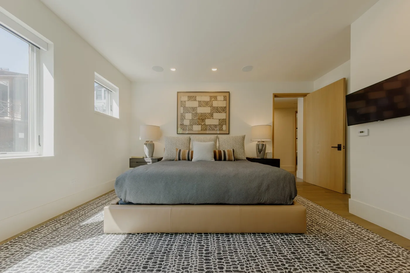 Un dormitorio con una cama grande, una alfombra estampada y ventanas en una pared.