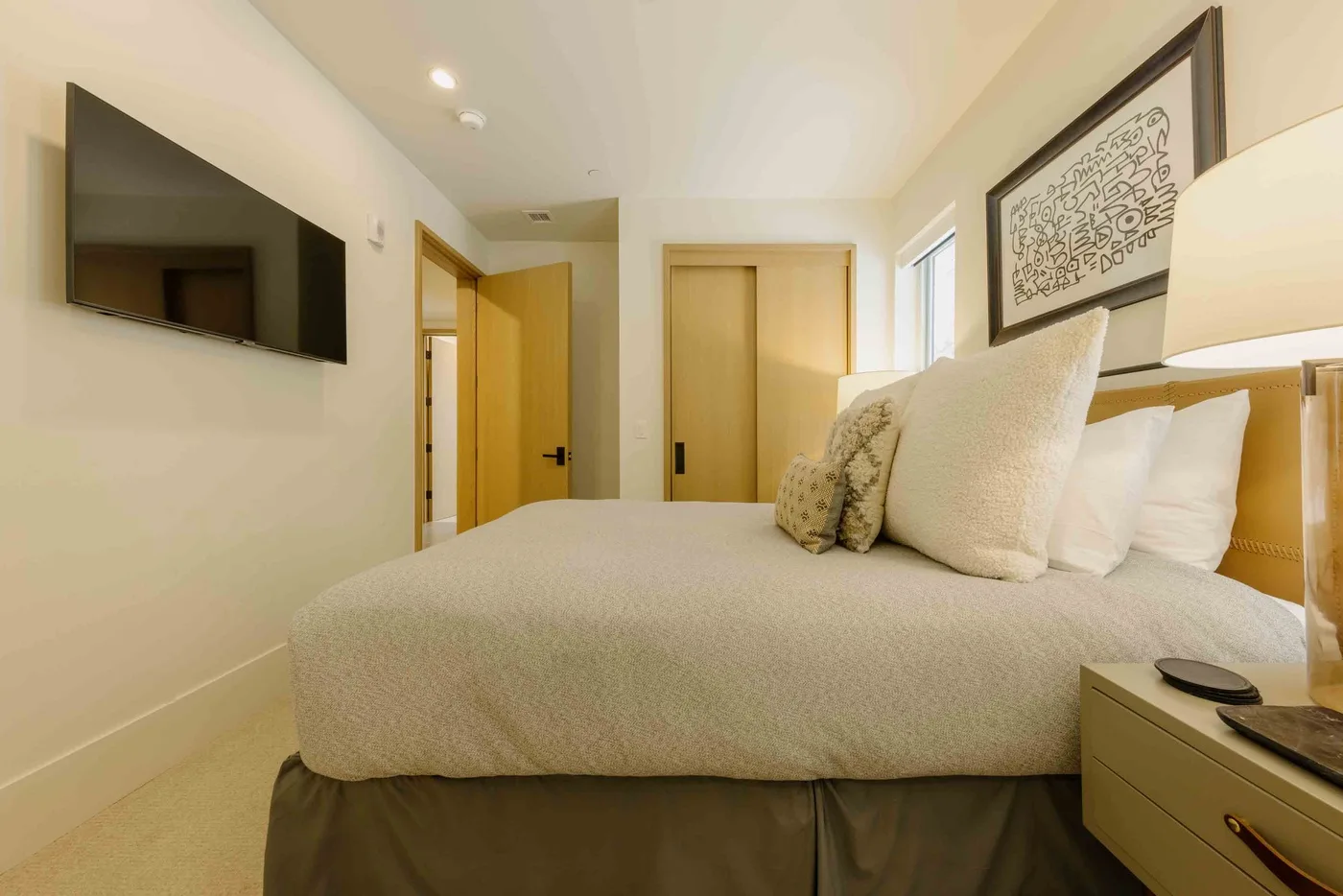 Un dormitorio con una cama tendida, un televisor en la pared y una obra enmarcada.