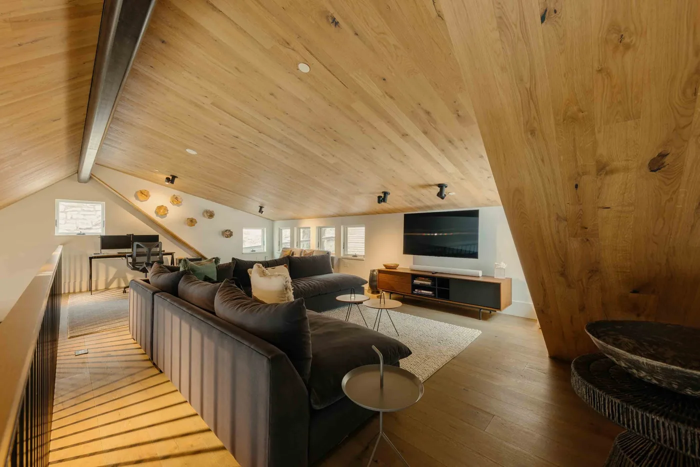 Una sala tipo loft con asientos oscuros, un televisor y techos inclinados de madera.