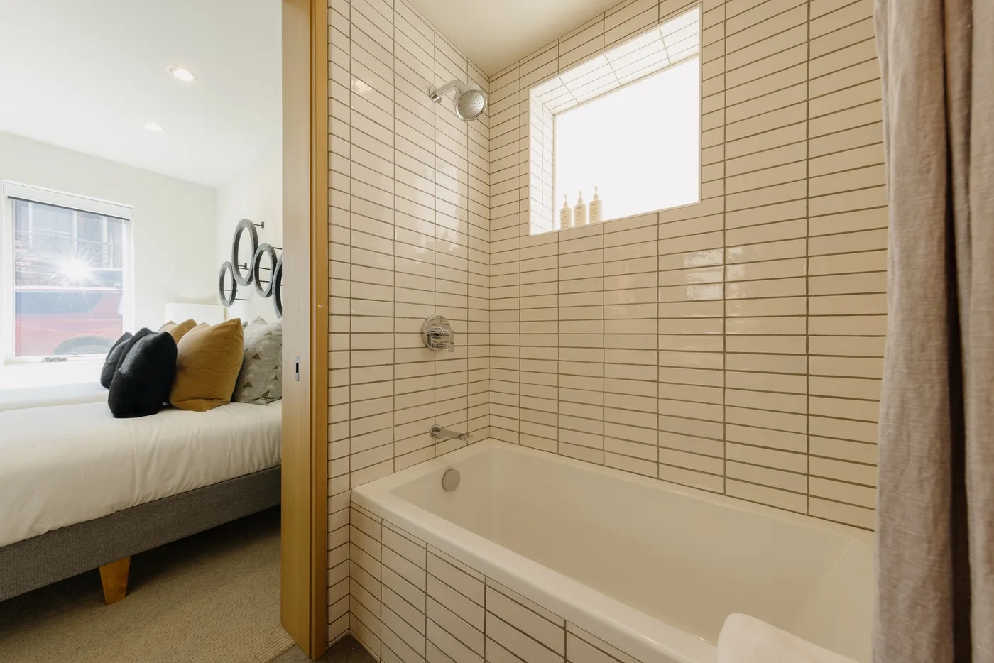 Un baño alicatado con bañera está junto a un dormitorio.