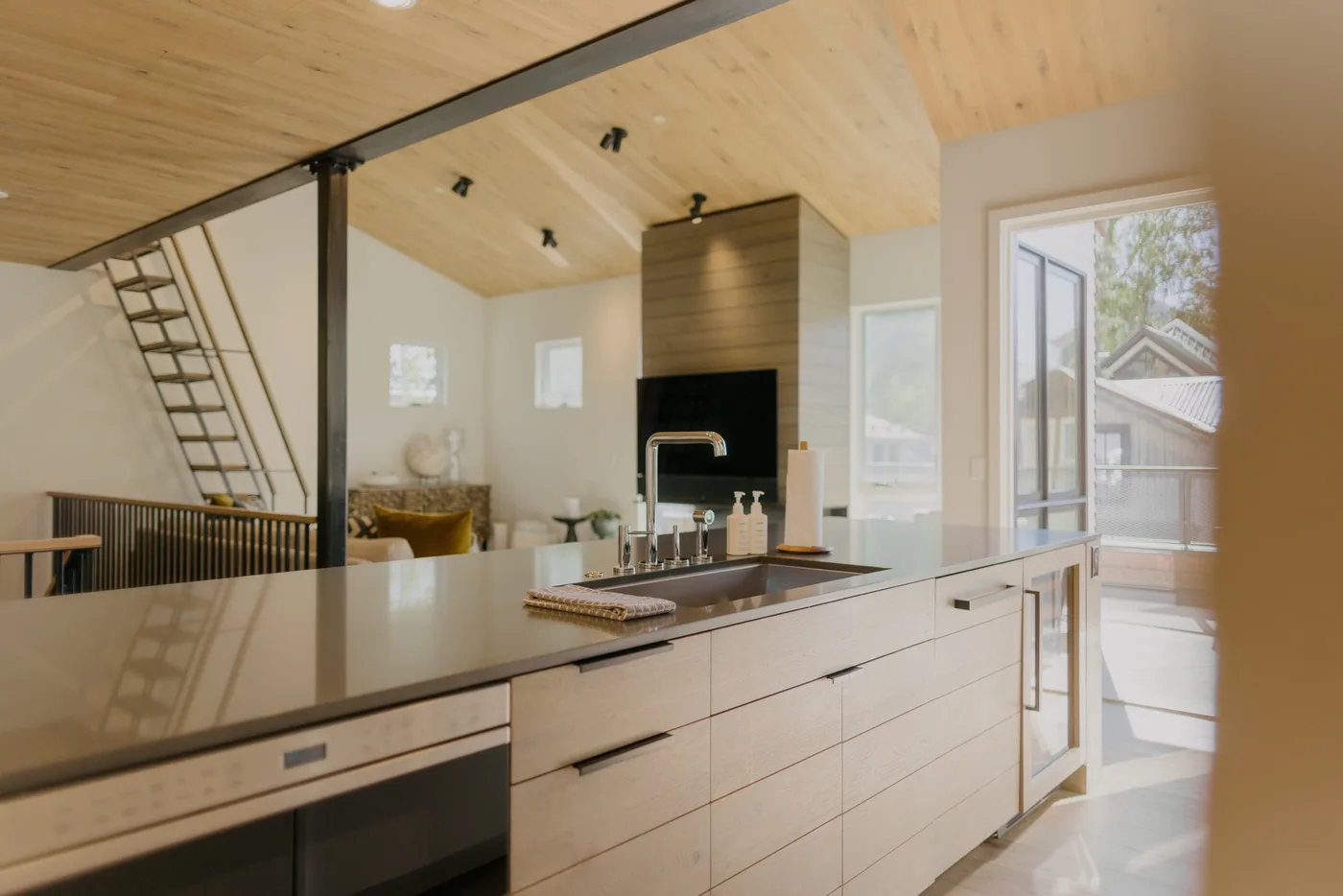 Una cocina luminosa con una isla larga y un fregadero bajo un techo inclinado de madera.