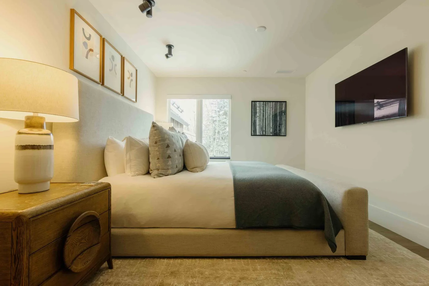 Un dormitorio con una cama bien tendida, cojines decorativos y un televisor montado en la pared.