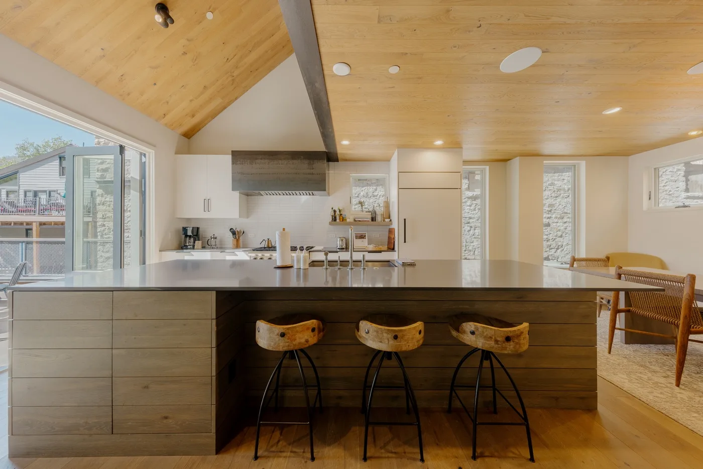Una cocina moderna con una gran isla y varios taburetes bajo un techo de madera.
