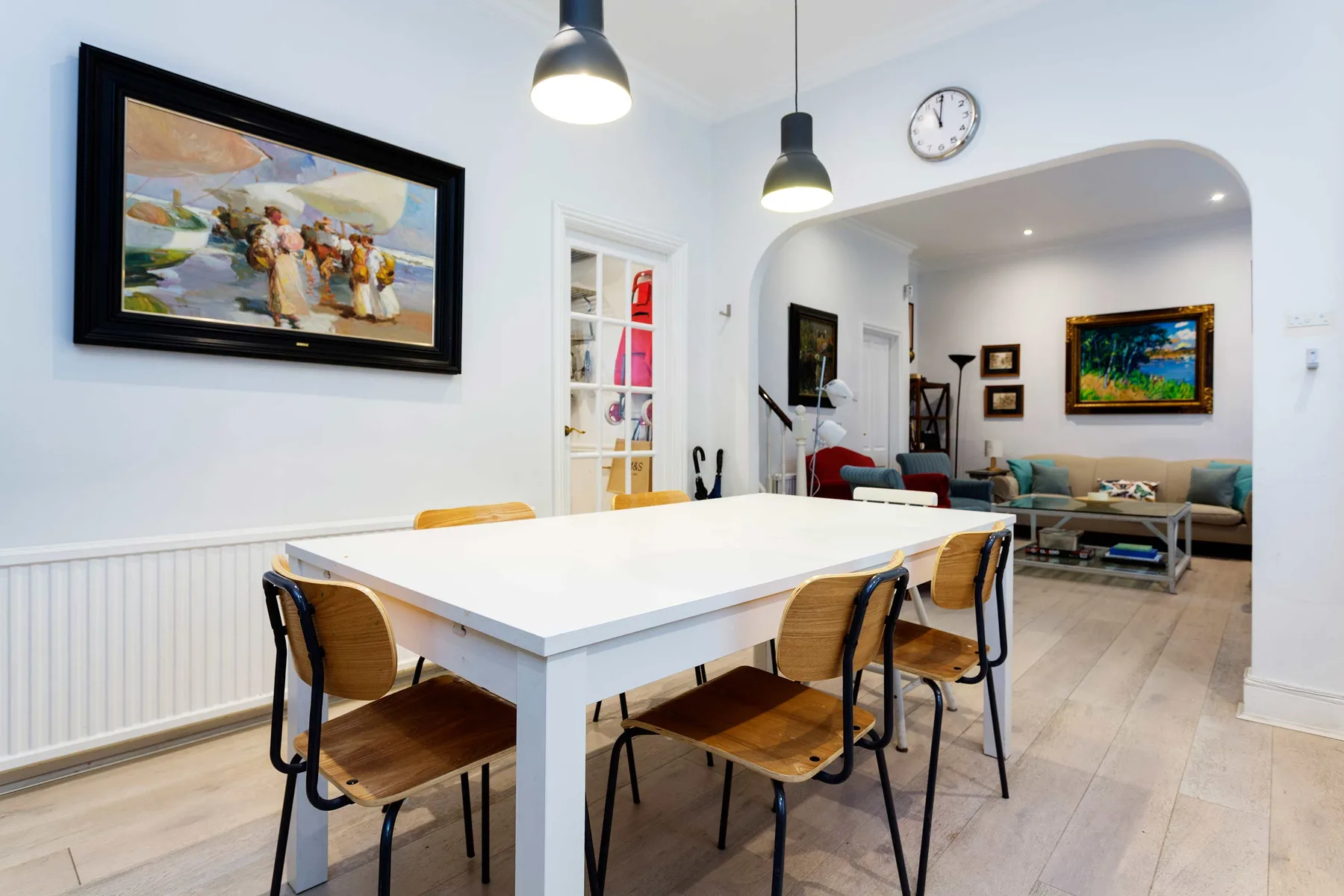 A dining area with a white table and seating opens onto a living area.