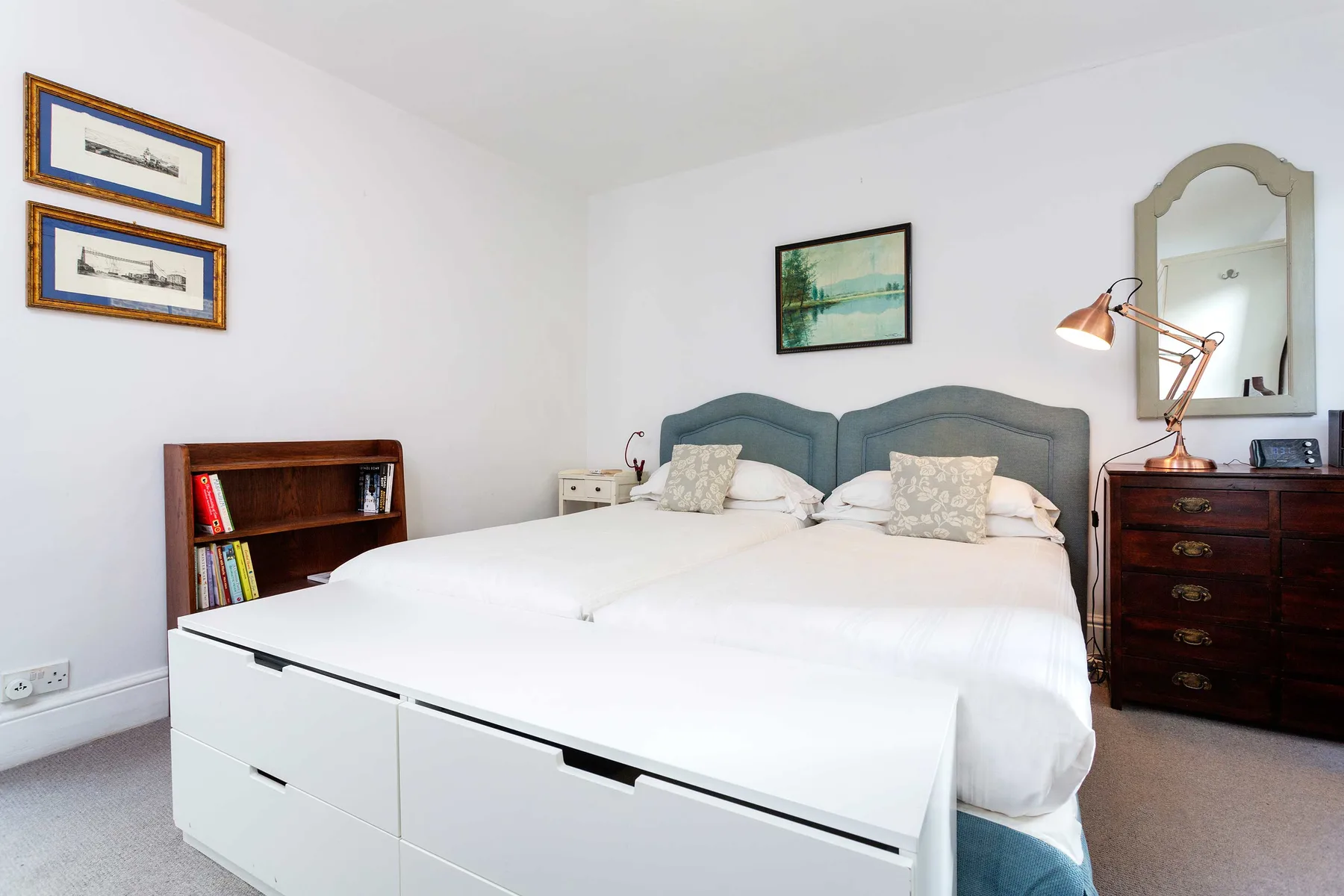 Un dormitorio luminoso con una cama grande, cuadros enmarcados y muebles de madera.