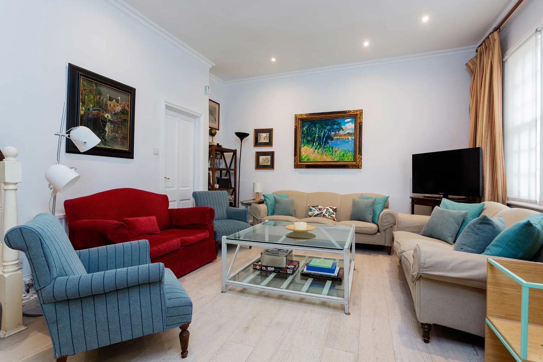 A bright living room with colorful seating, a glass coffee table, and framed artwork.