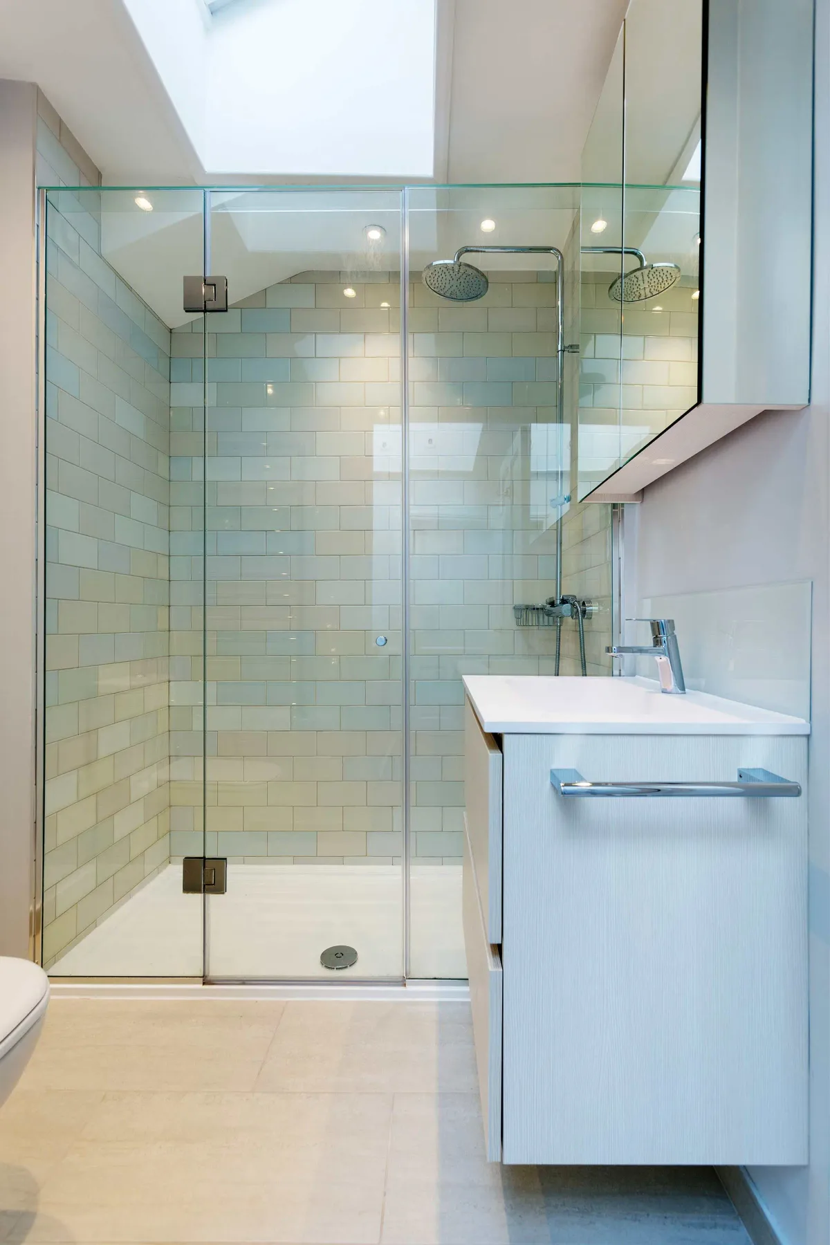 Un baño luminoso con una ducha de vidrio y un tocador.