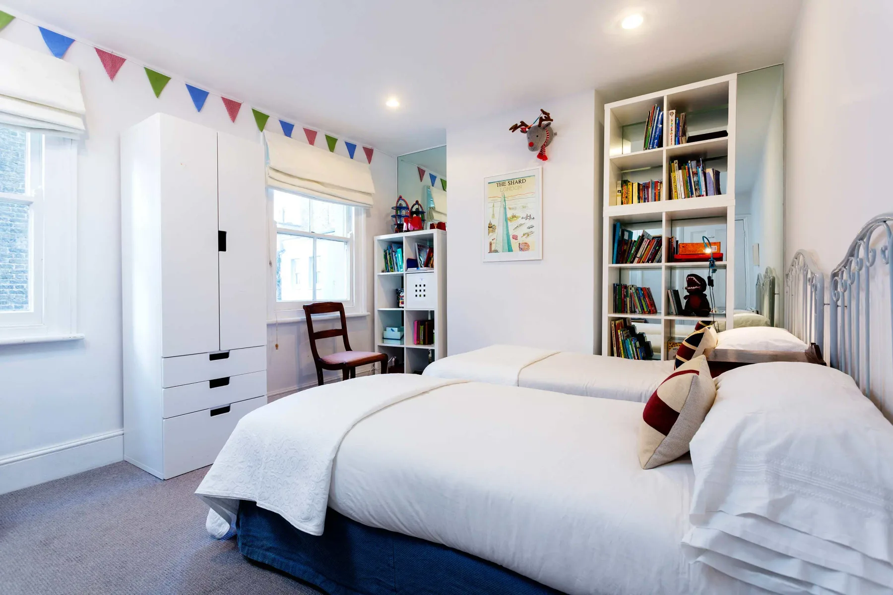 Un dormitorio luminoso con ropa de cama blanca, estanterías y banderines de colores.