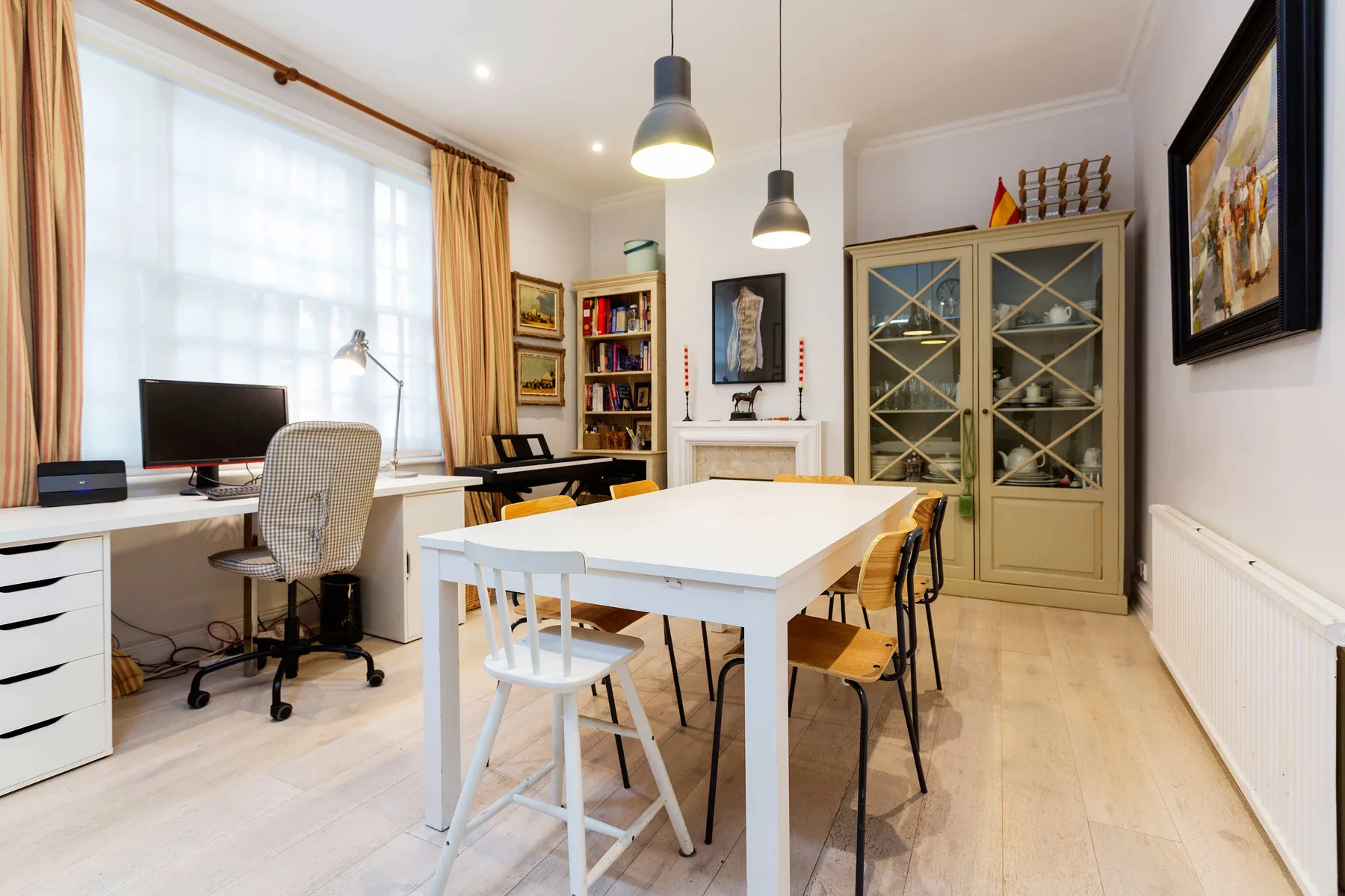 A bright study and dining area with a large table, desk, and glass-front cabinets.
