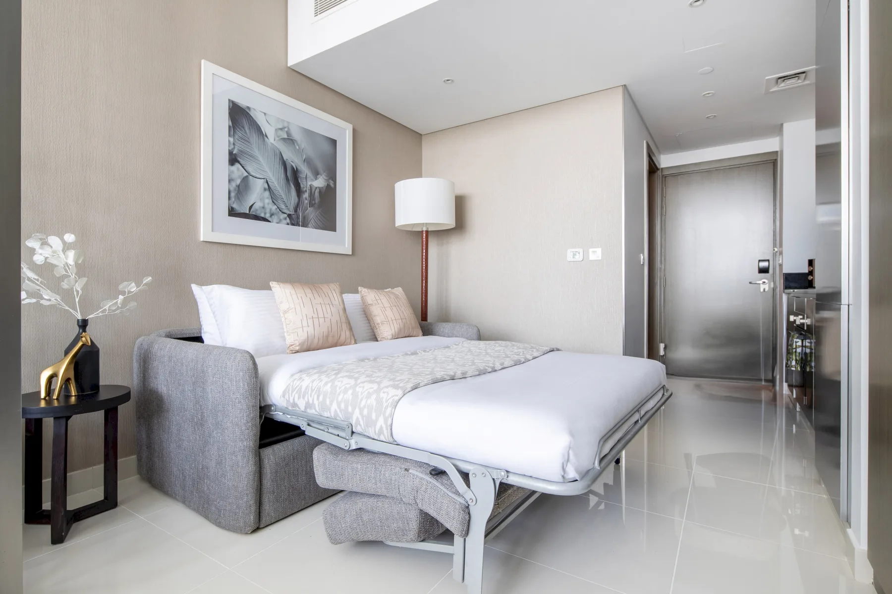 Un dormitorio con una cama, asientos grises y una obra enmarcada en la pared.
