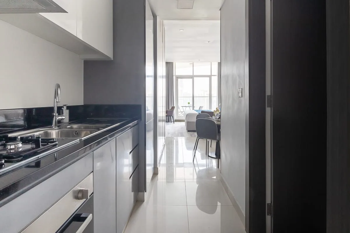 Una cocina estrecha se abre a un comedor luminoso con mesa y sillas.