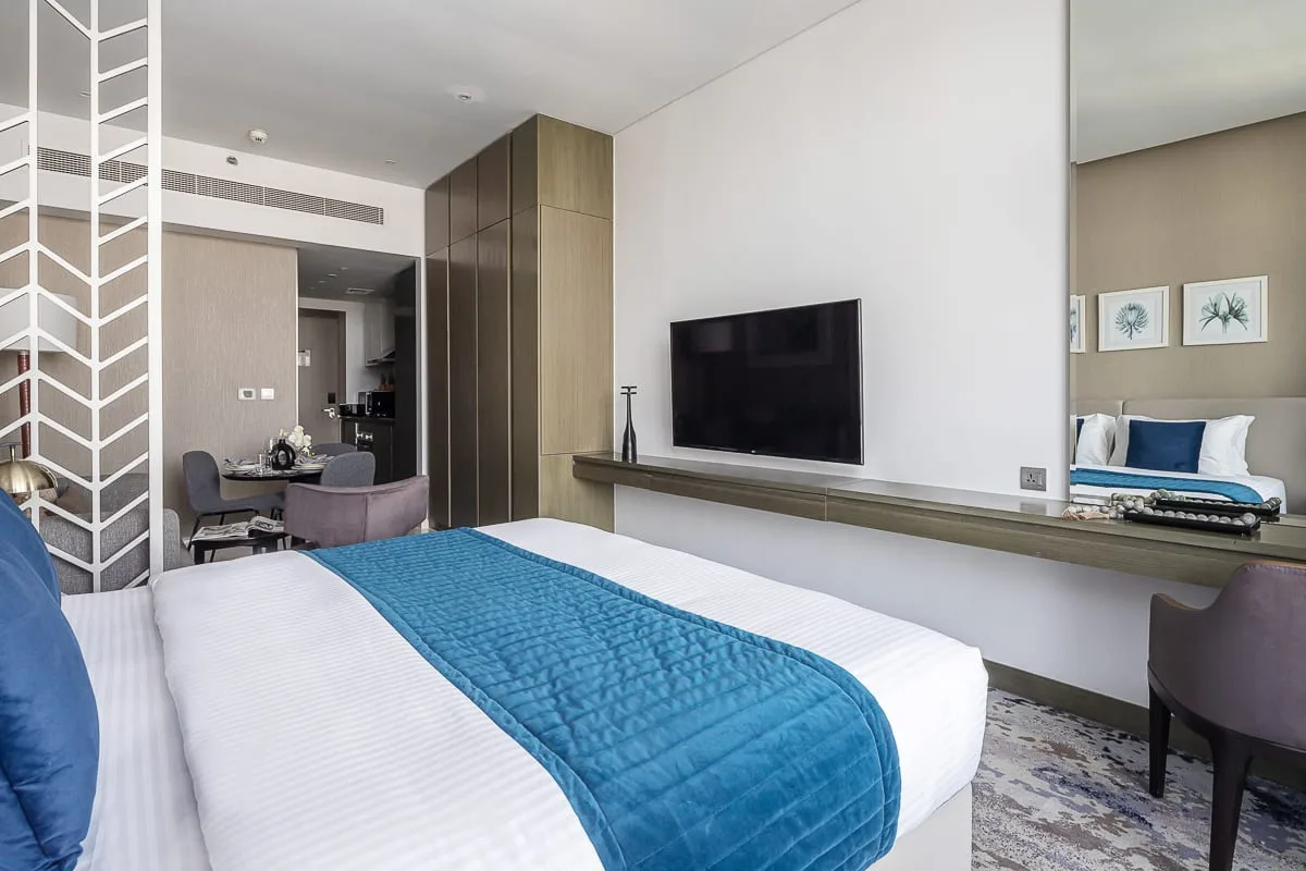 Un dormitorio moderno con una cama, ropa de cama azul y un televisor en la pared.