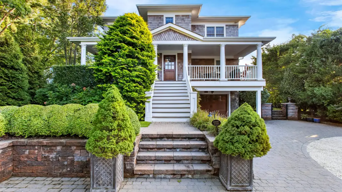 Una casa grande con un porche cubierto y un jardín ajardinado.
