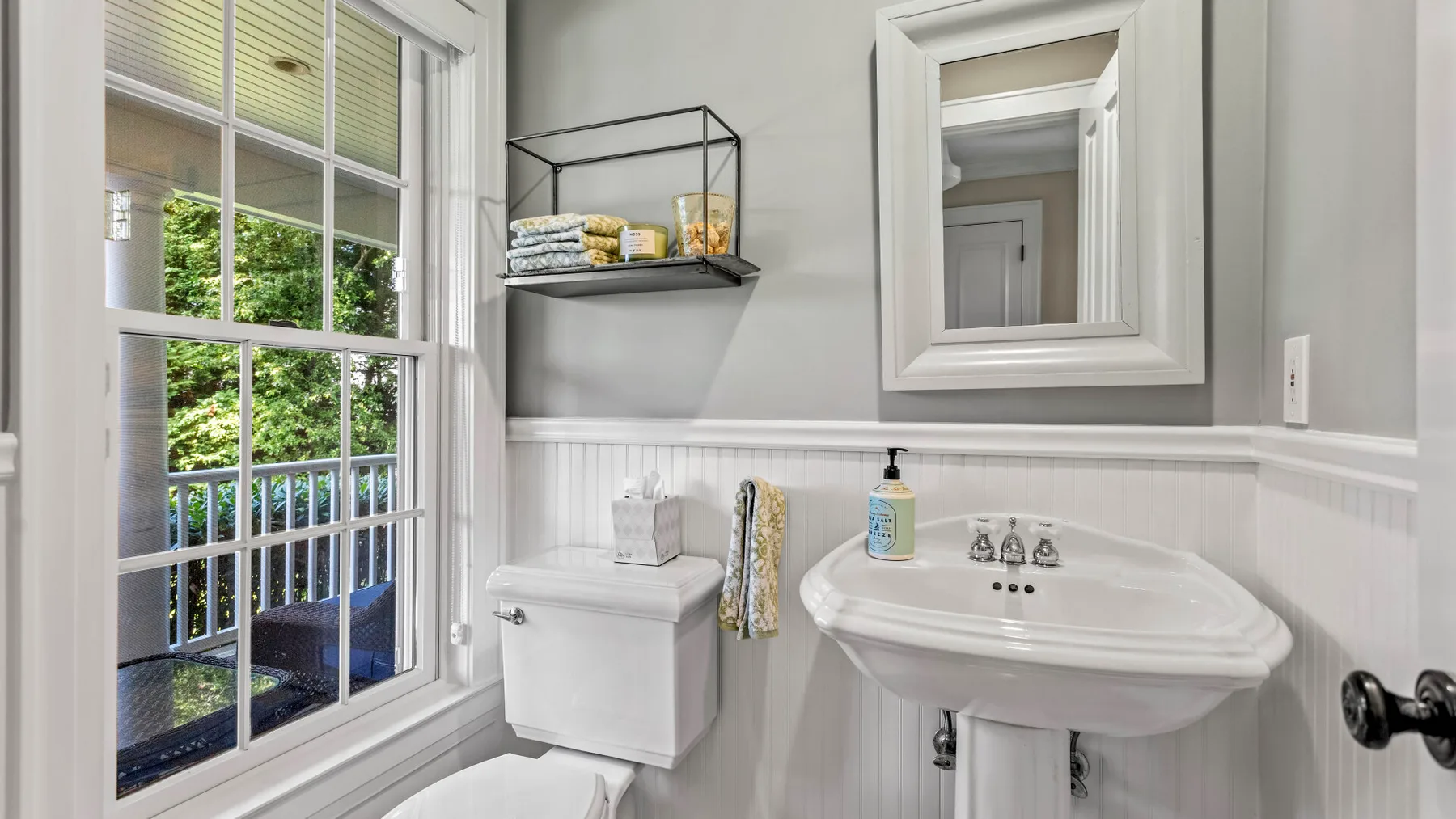 Un baño luminoso con lavabo de pedestal y una ventana grande con vistas a la vegetación.