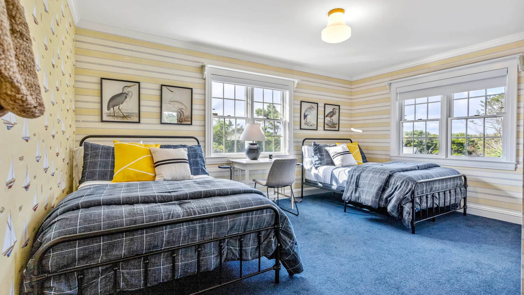Un dormitorio con dos camas, alfombra azul y ventanas grandes.