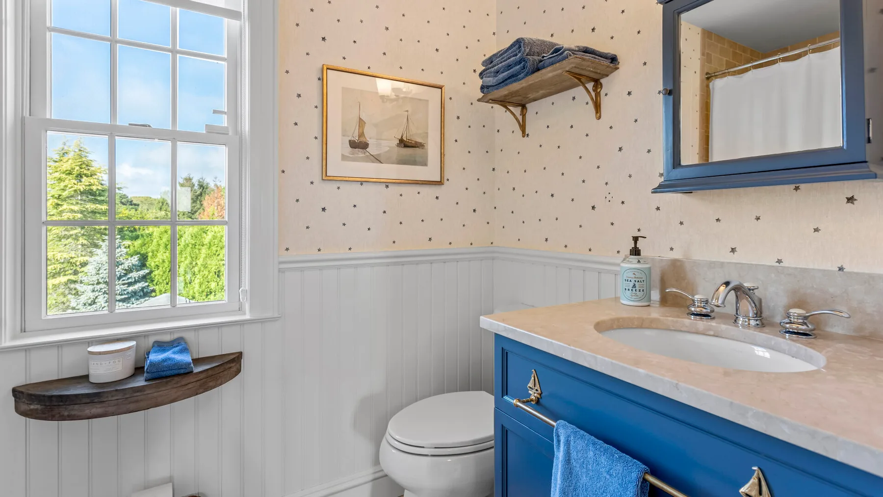 Un baño con tocador azul, lavabo, inodoro y una ventana grande.