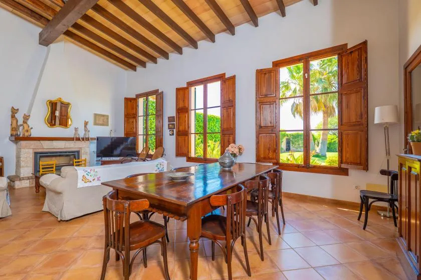 Un comedor y sala de estar con una mesa de madera y grandes ventanas.
