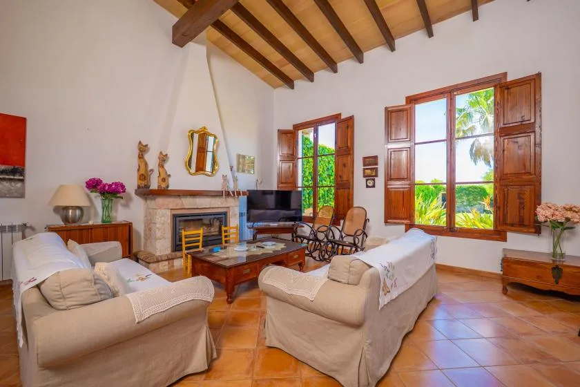 Una sala de estar con asientos, una chimenea y grandes ventanas con marcos de madera.