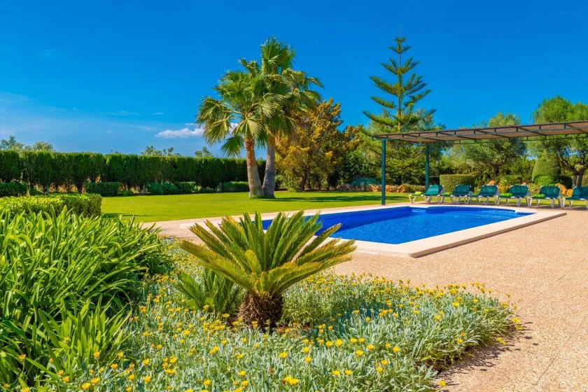 Una piscina al aire libre junto a un jardín y una zona de asientos con sombra.
