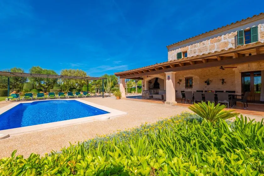 Una piscina exterior está junto a una casa de piedra y un patio sombreado.
