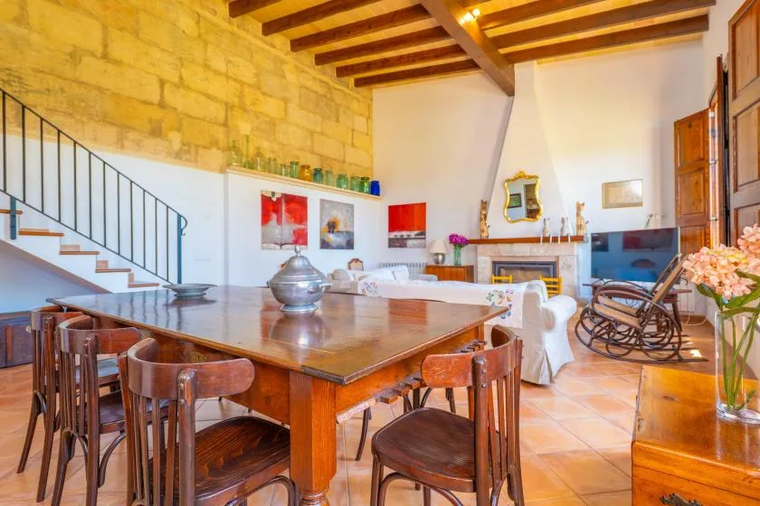 Un comedor y sala de estar con una mesa grande de madera y vigas vistas en el techo.